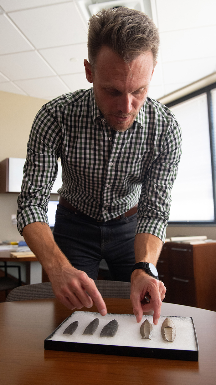 A man sorts through a collection of stone spear points.