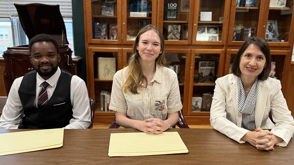 A man and two women sit at a table in a library with file folders in front of  them.