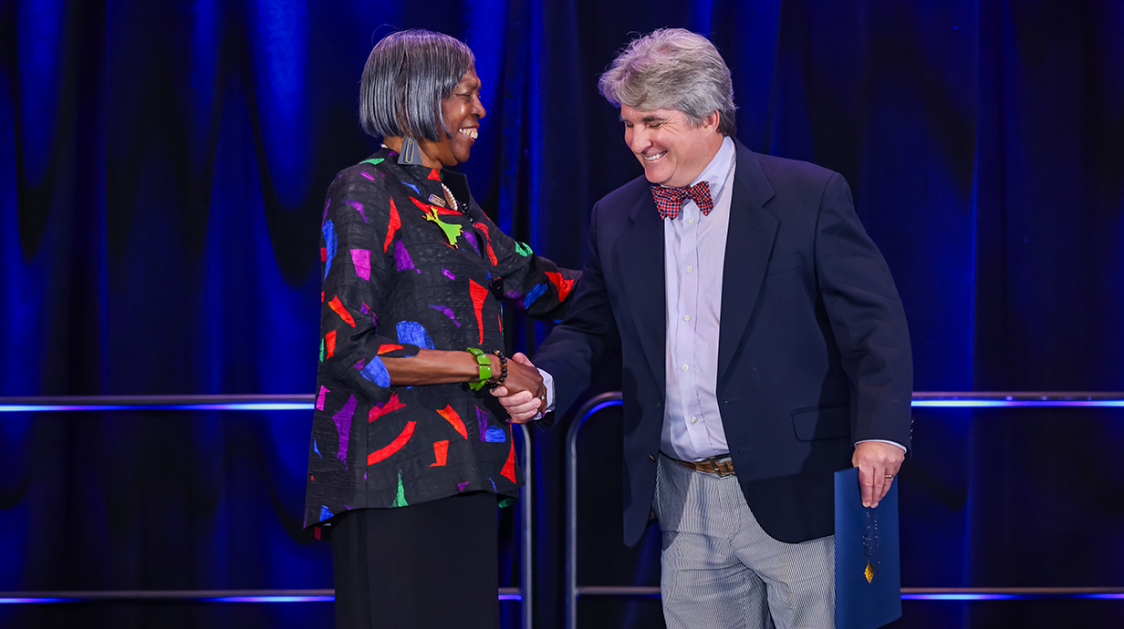 A woman presents an award certificate to a man on a stage.