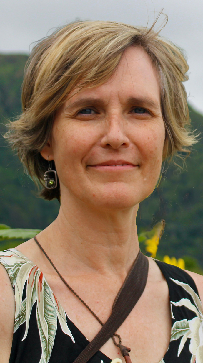 Headshot of a woman wearing a floral print dress and standing in front of a mountain.