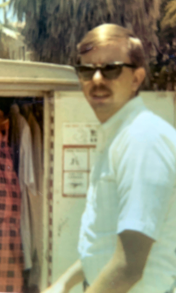 A young man stands behind a small trailer loaded with clothing.