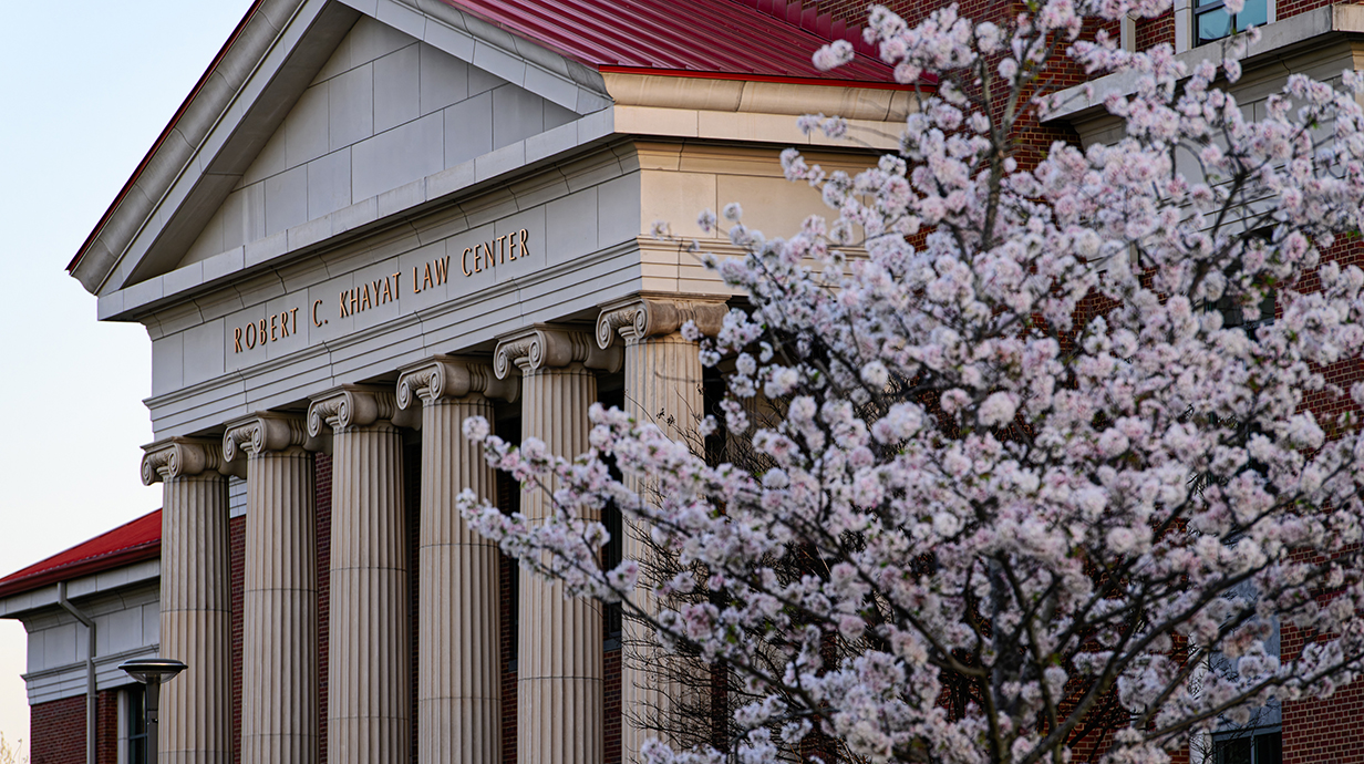 Flowering trees frame a large brick building with white columns.