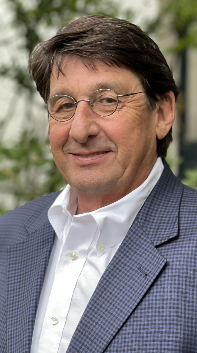 Headshot of a man wearing a blue plaid jacket over a white dress shirt.
