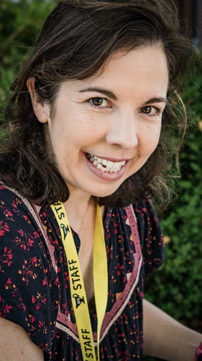 Headshot of a woman wearing a floral print dress and a yellow 'Staff' lanyard around her nect.