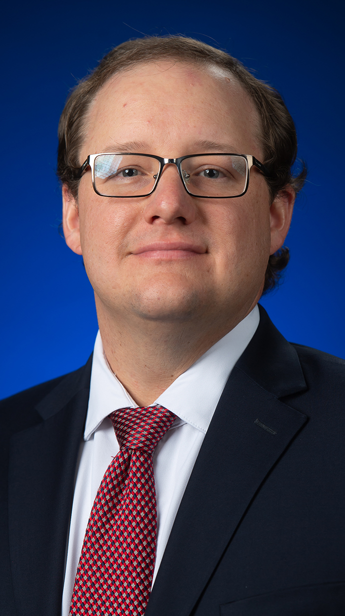 Headshot of a man wearing glasses and a dark blue suit with a red tie.