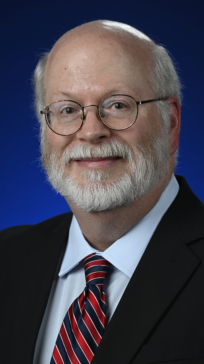Headshot of a man wearing glasses and a dark suit and a red tie.