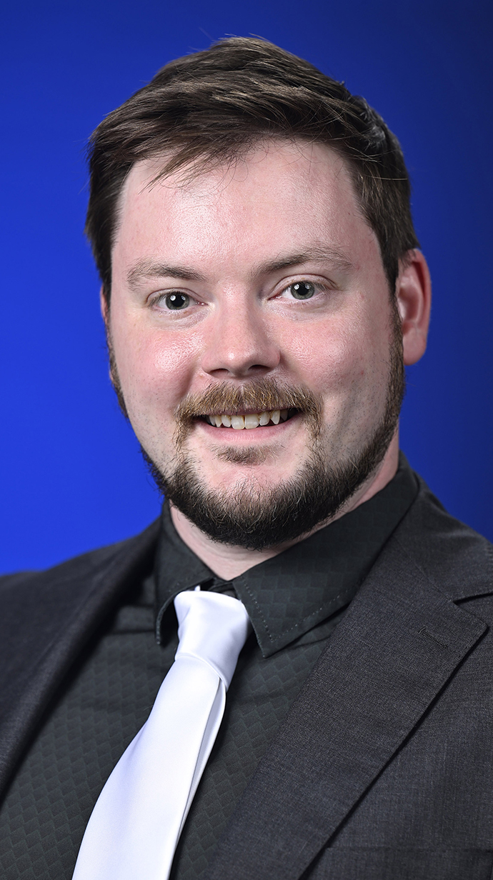 Headshot of a man wearing a black shirt and a white tie.