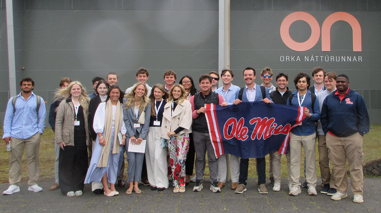 A large group of young people holding an Ole Miss flag stand in front of a large building with 'ON' on its facade.