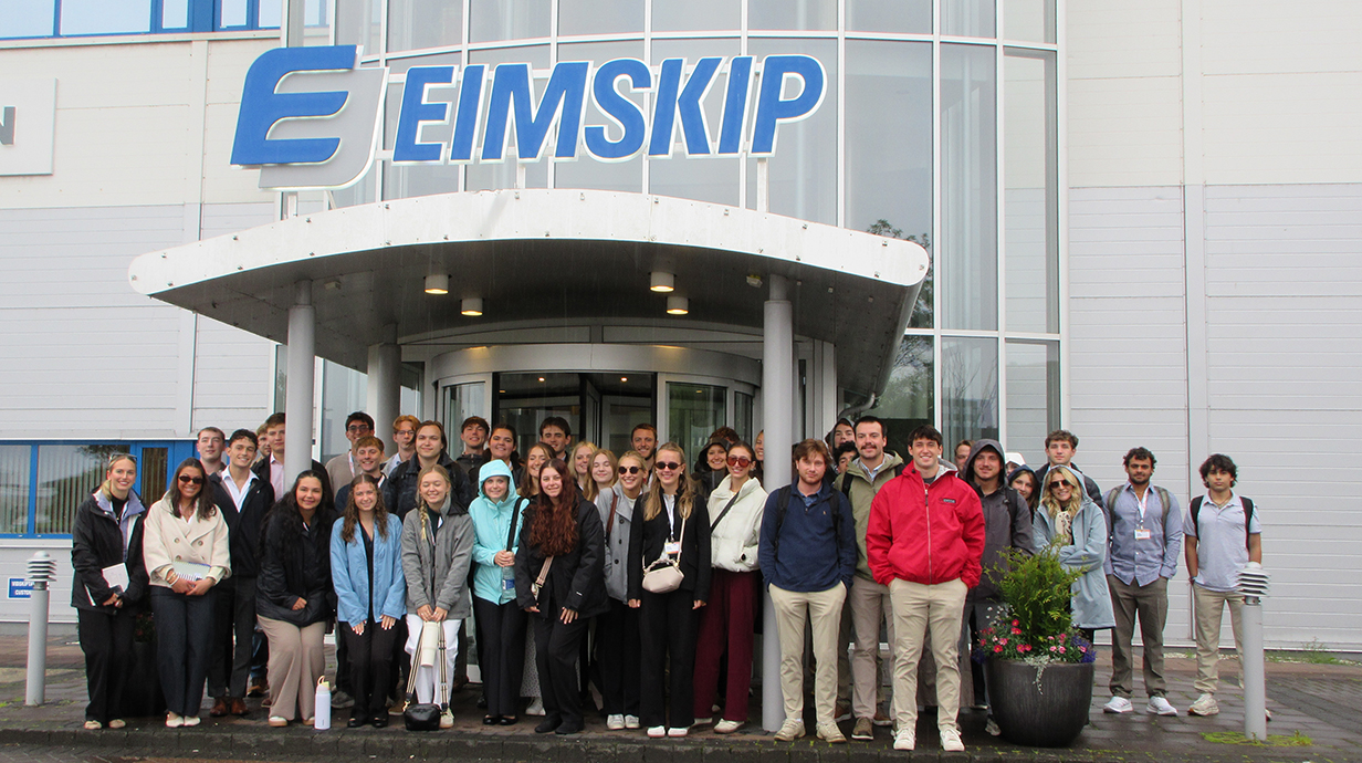 A large group of young people stands under an awning on a large modern building with the name 'EIMskip' above them.