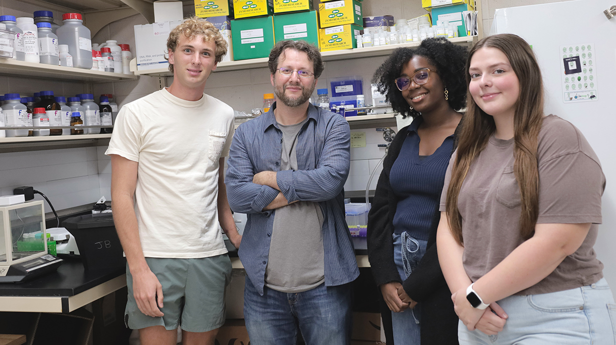Two men and two women stand in a biology laboratory.