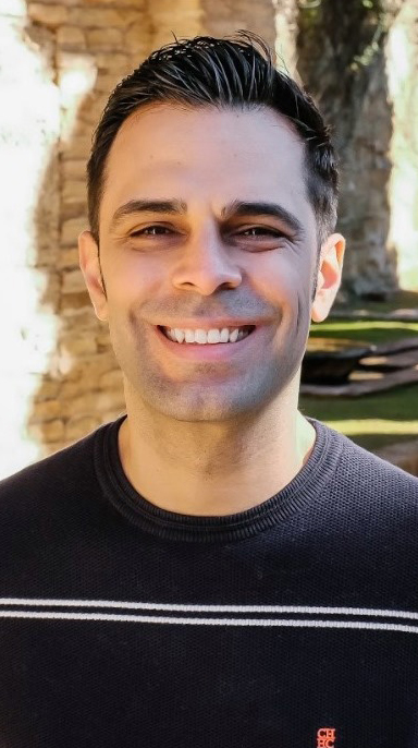 Headshot of a man wearing a black sweater with thin white stripes.