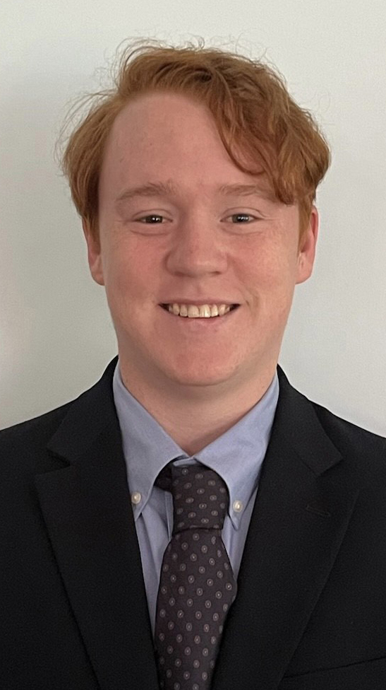 Headshot of a young man wearing a dark suit and a patterned tie.