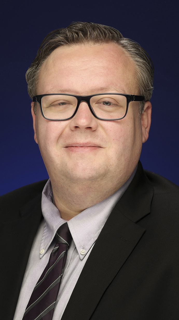 Headshot of a man wearing glasses and a dark suit.