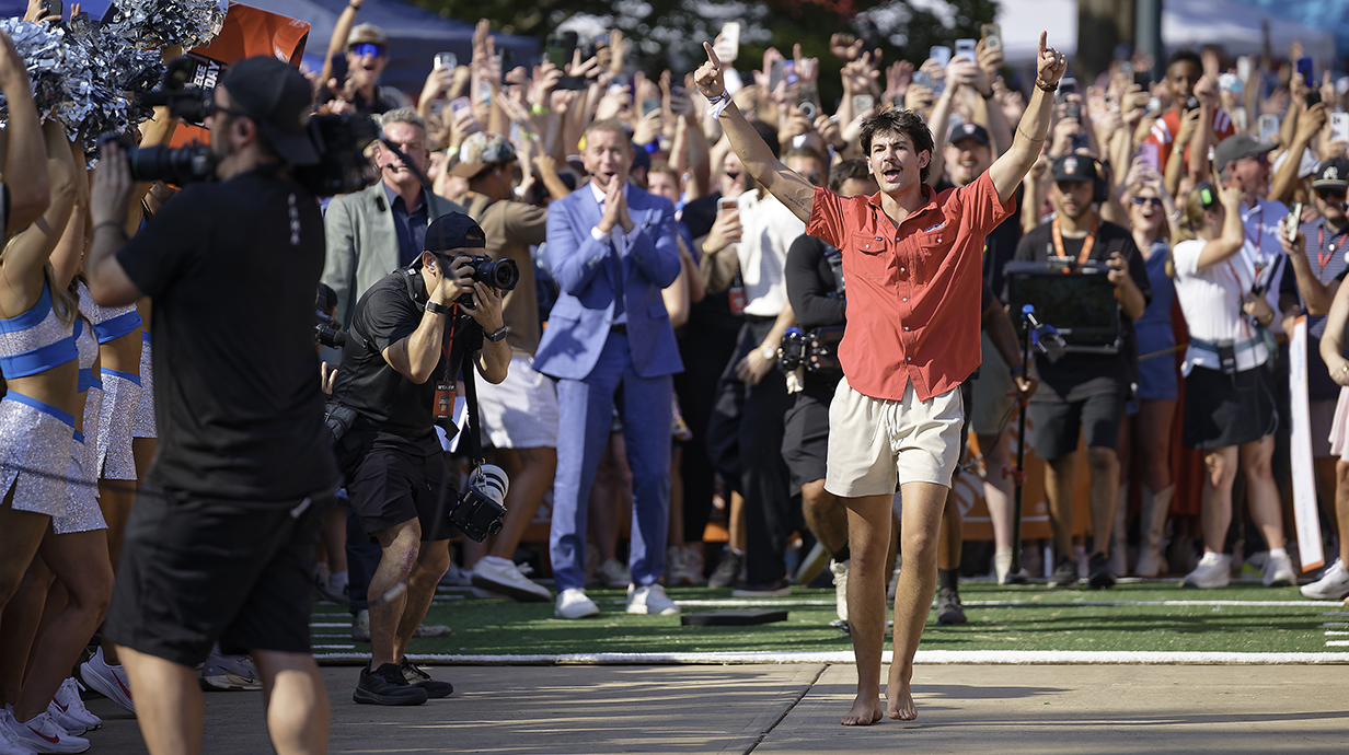 A young man raises his arms in celebration as a large crowd behind him cheers.