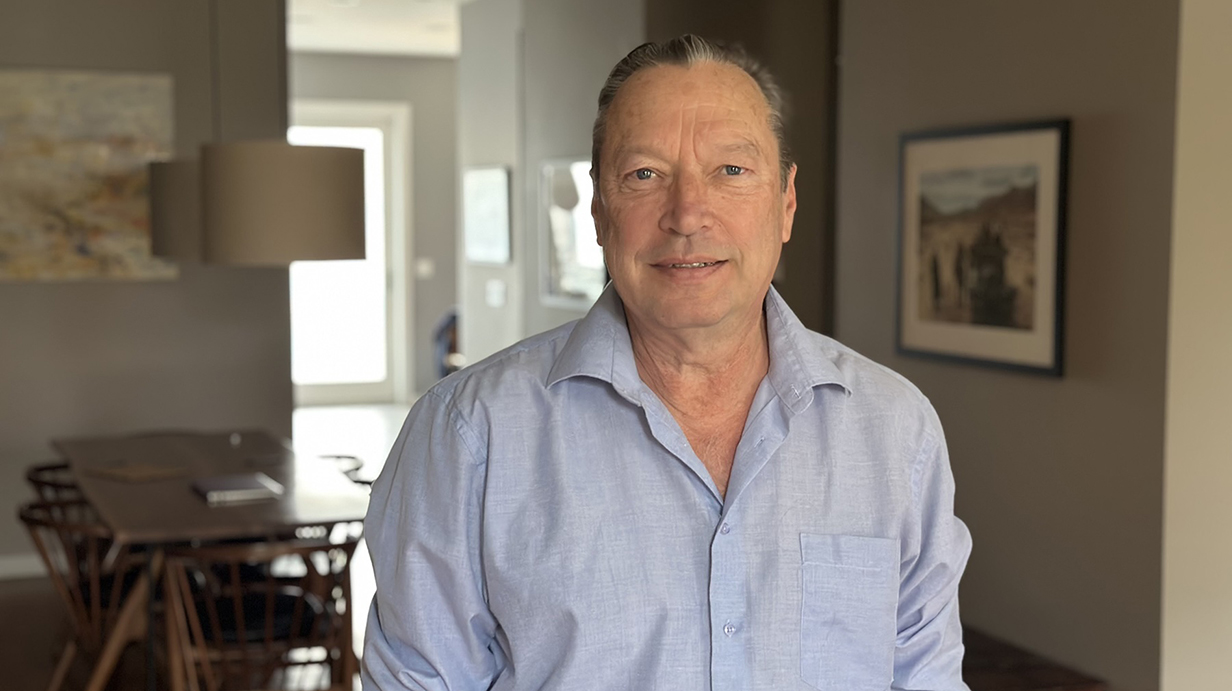A man wearing a light blue shirt stands in an apartment.