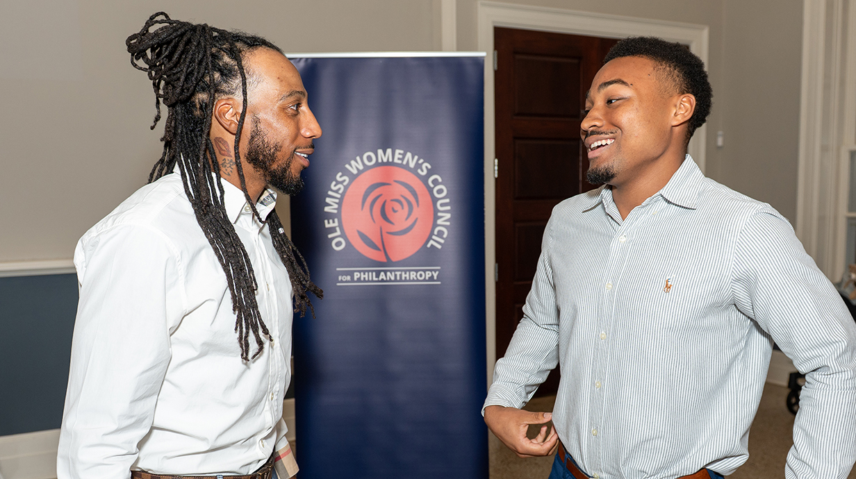 Two young men talk while standing in a lobby.