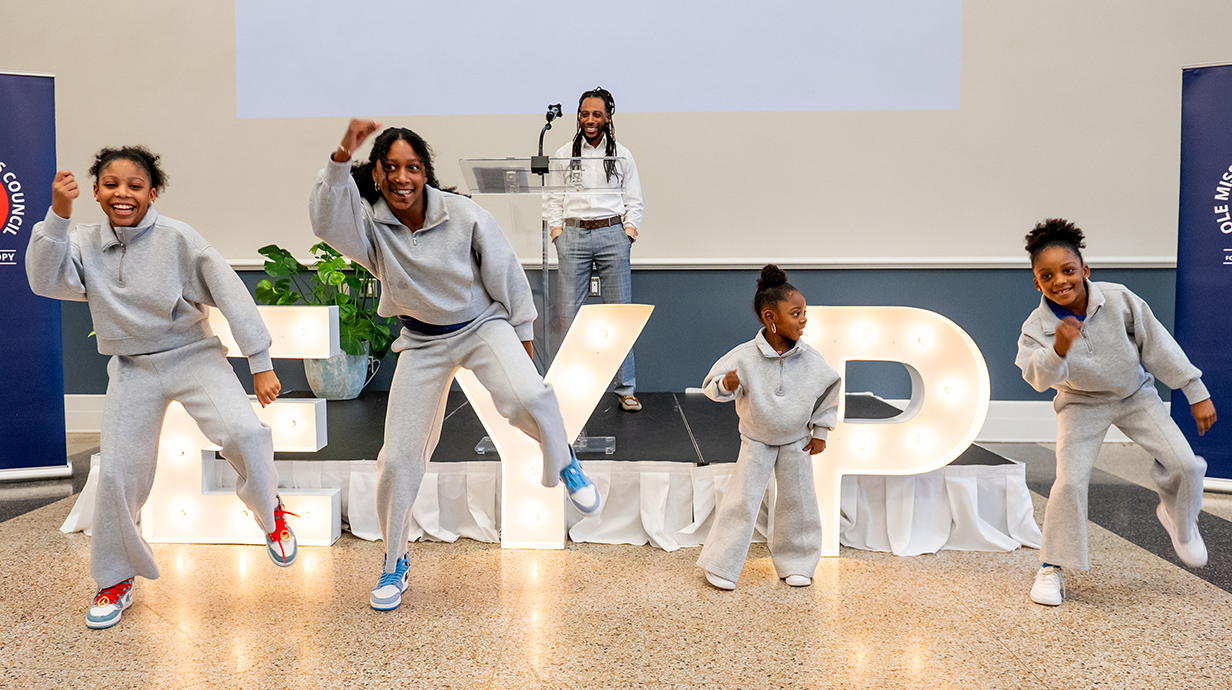 Four young girls perform a dance routine in front of a podium.