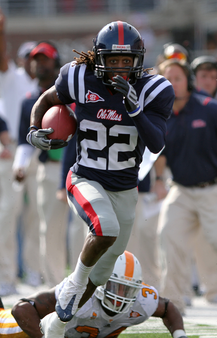 A football player with teh ball outruns a defender in a stadium.
