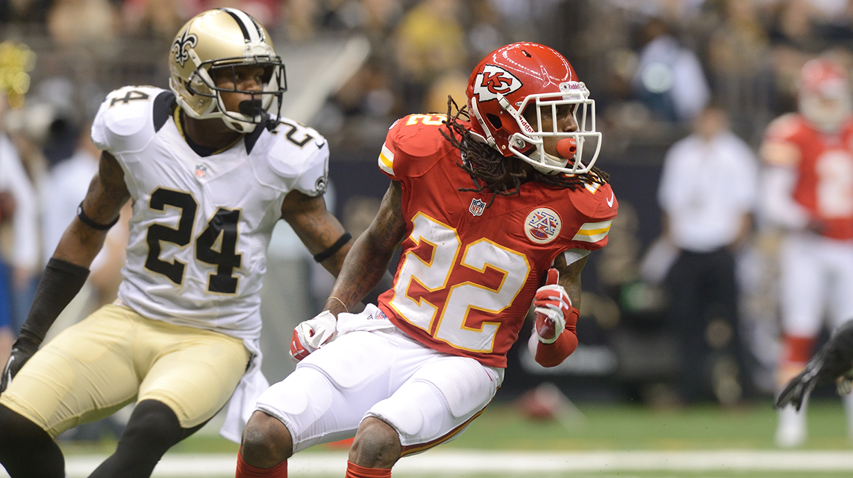Two football players change direction as they look off camera during a game in a stadium.