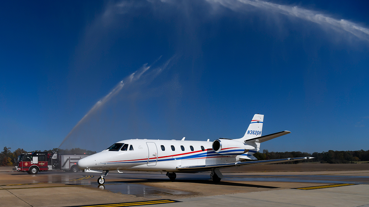 Two fire trucks provide a water cannon salute as a small jet taxis underneath.