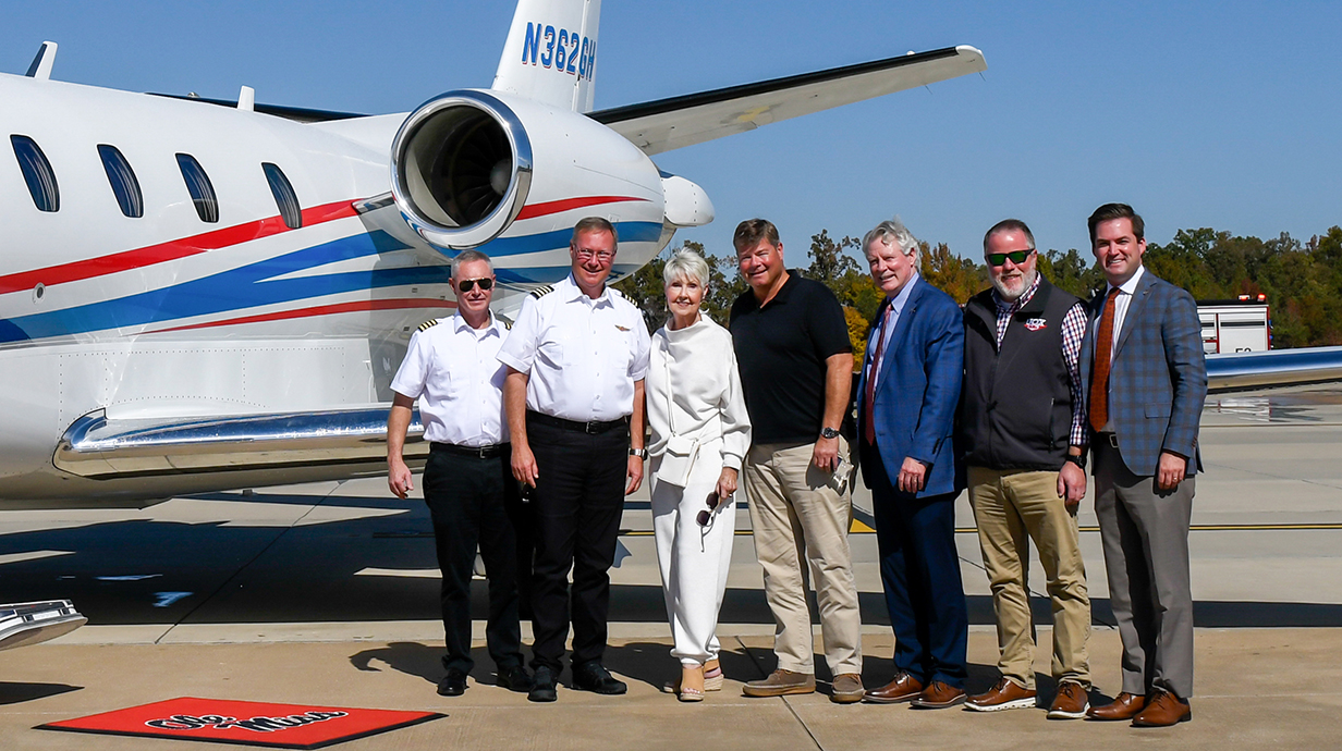 A group of people stands beside a small jet on an airport tarmac.