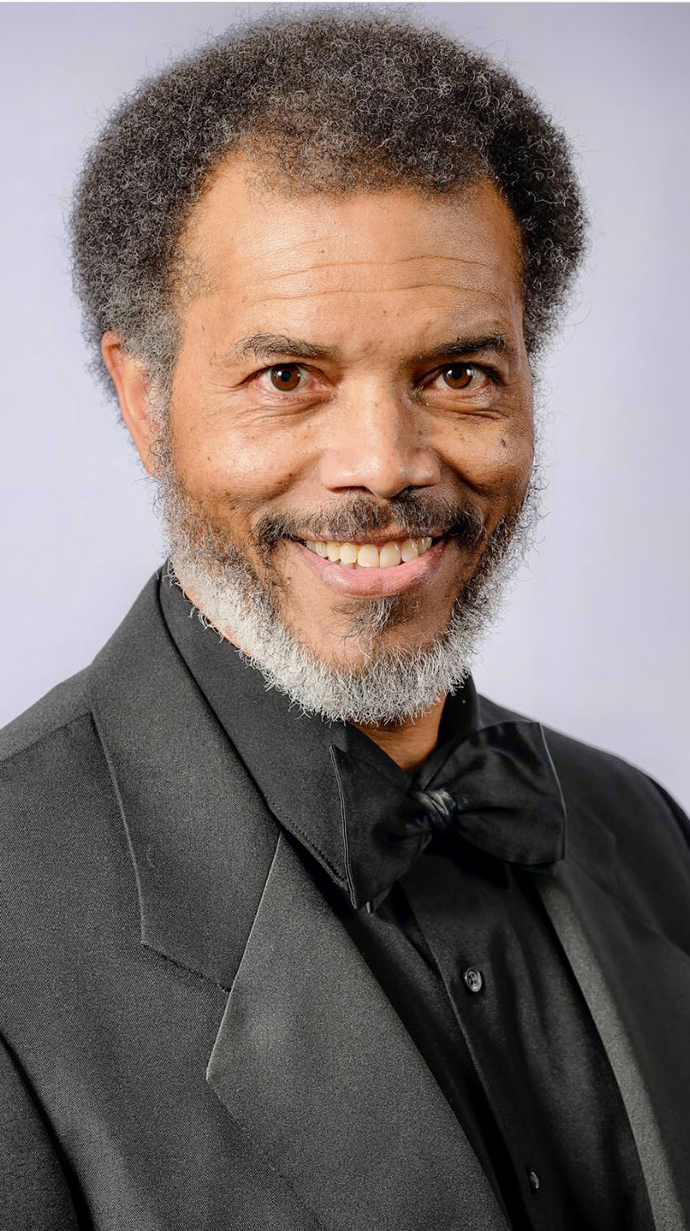 Headshot of a man wearing a gray suit with a black shirt and bowtie.