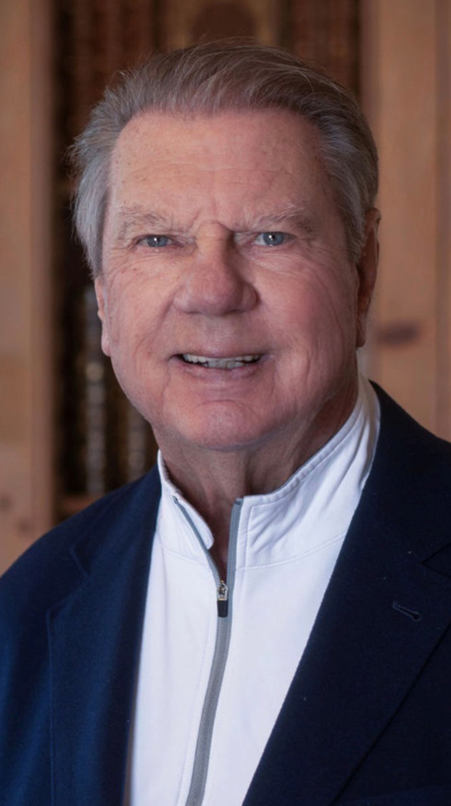Headshot of a man wearing a blue jacket over a white zippered shirt.