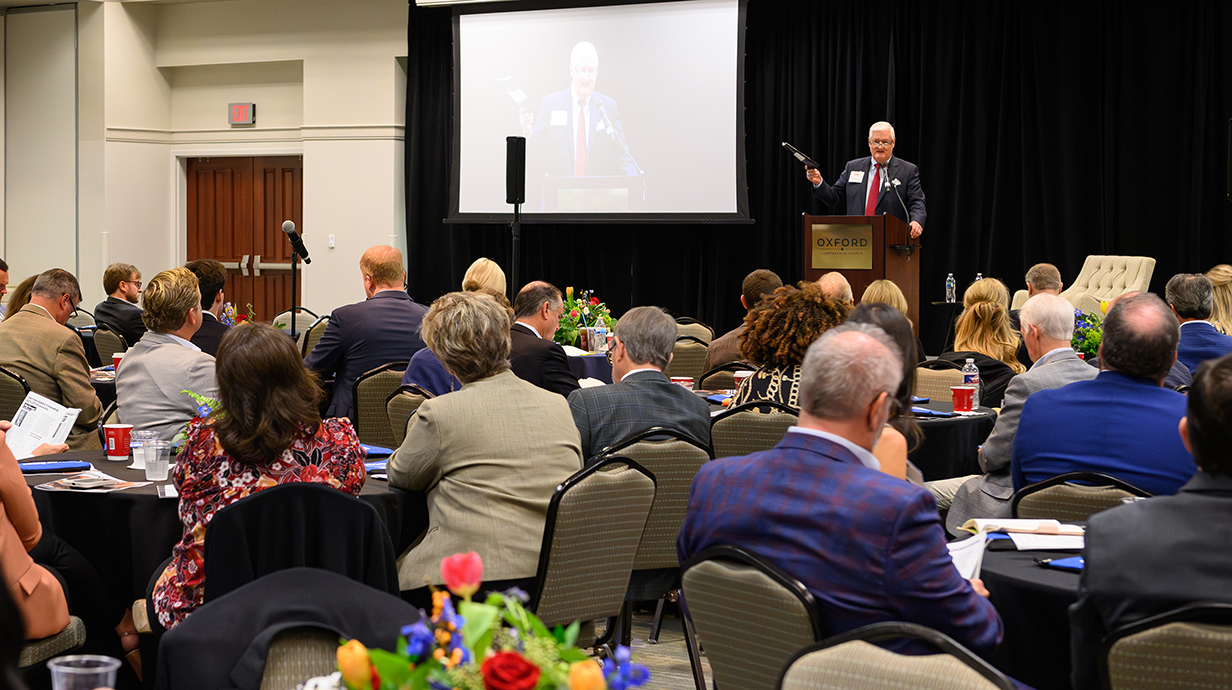 A man on a stage talks to a crowd seated in a conference hall.