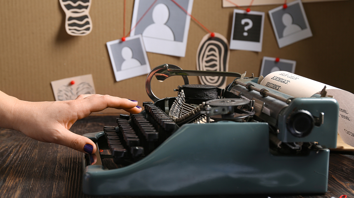 A woman's hand reaches toward a manual typewriter sitting in front of a bulletin board lined with photos and scraps of paper, all linked by strands of yarn.