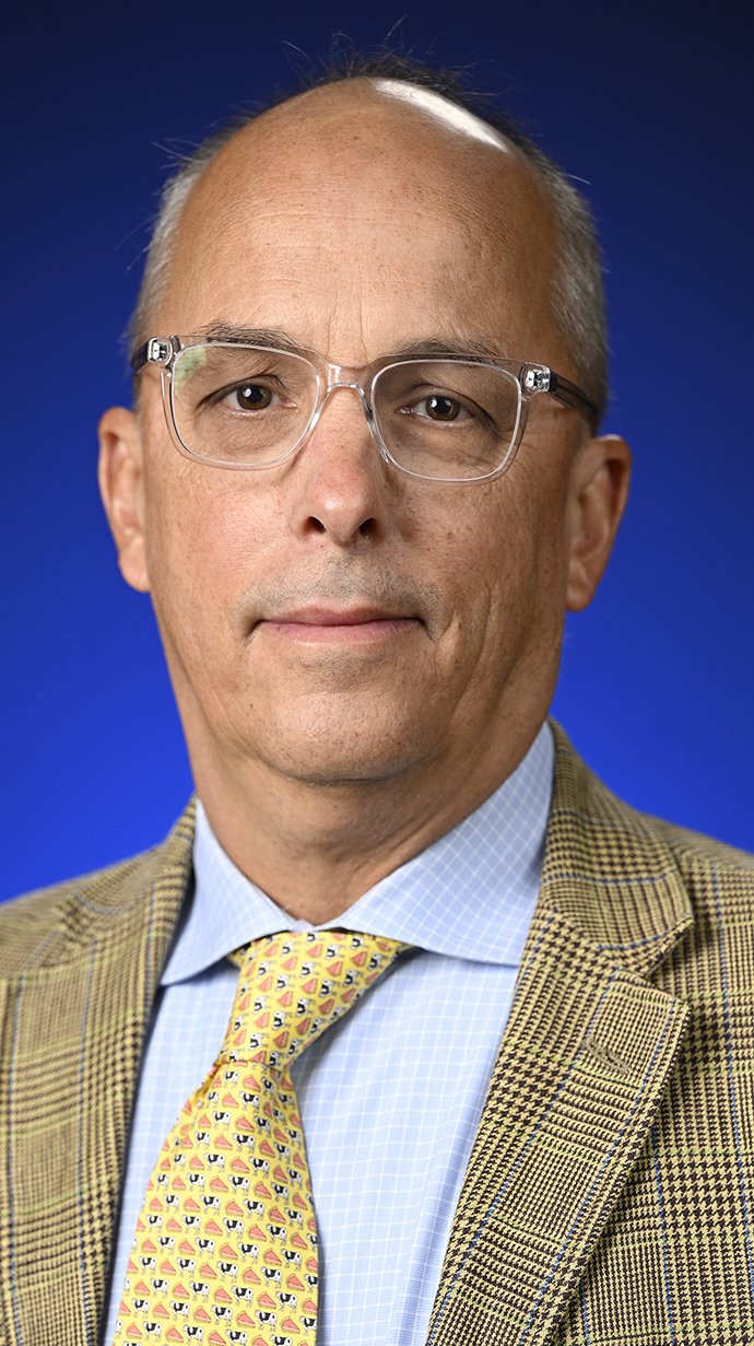 Headshot of a man wearing a tan plaid suit with a yellow tie.