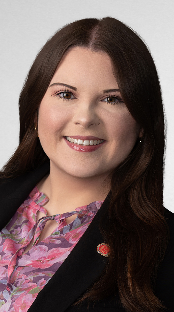 Headshot of a young woman wearing a black jacket over a reddish paisley blouse.