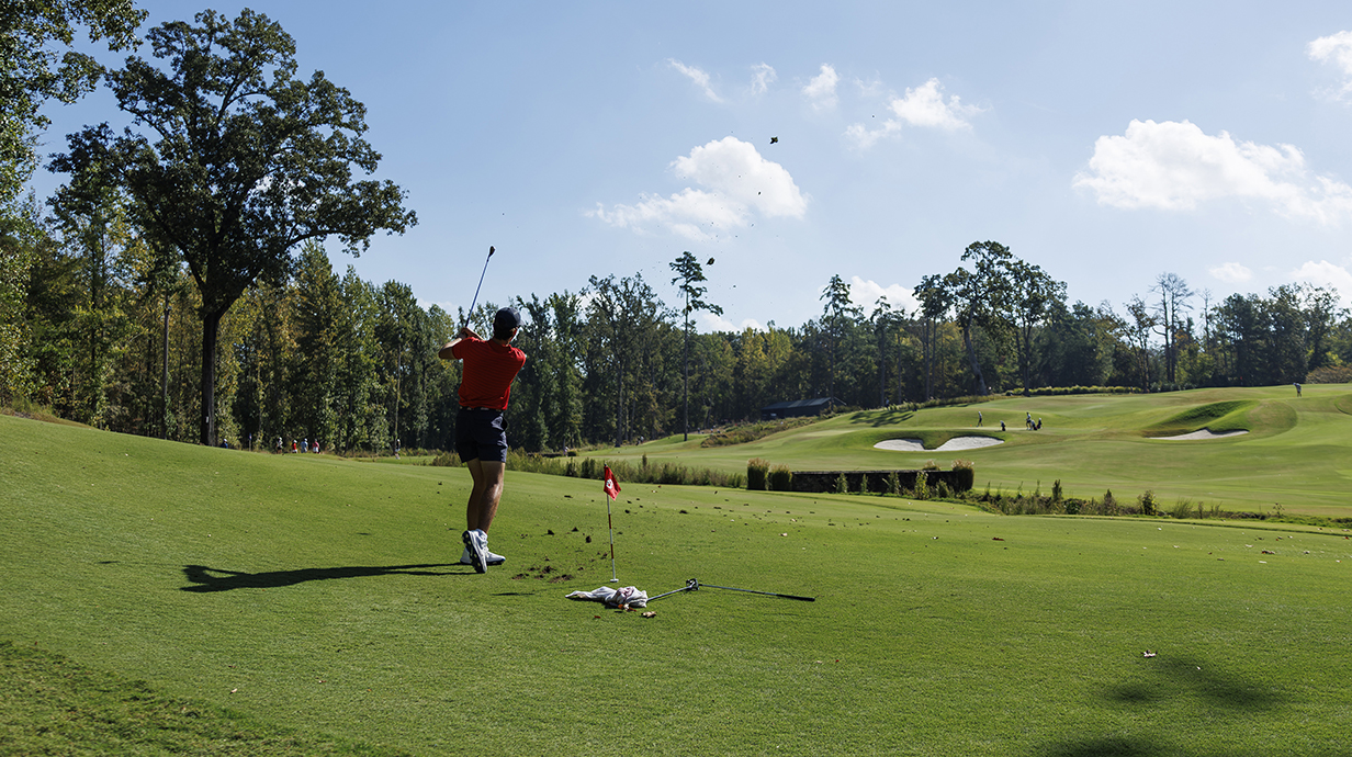 A young man tees off on a golf course on a sunny day.