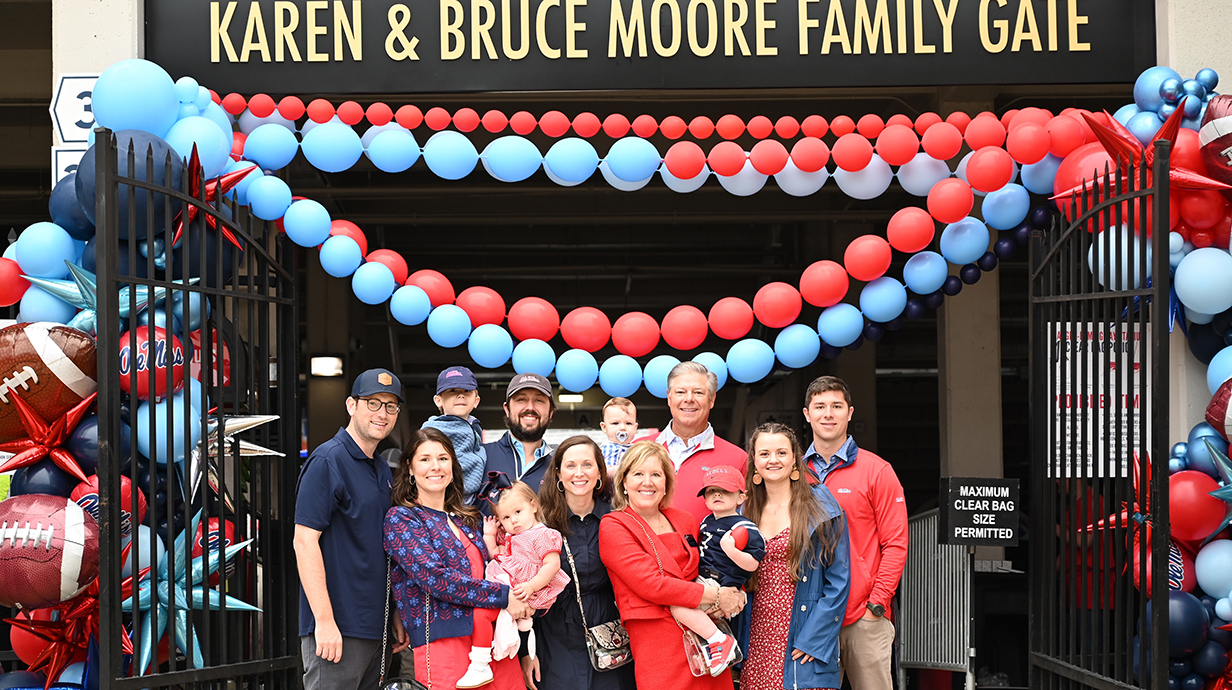 A group of people stands in front of an entrance gate draped in balloons.