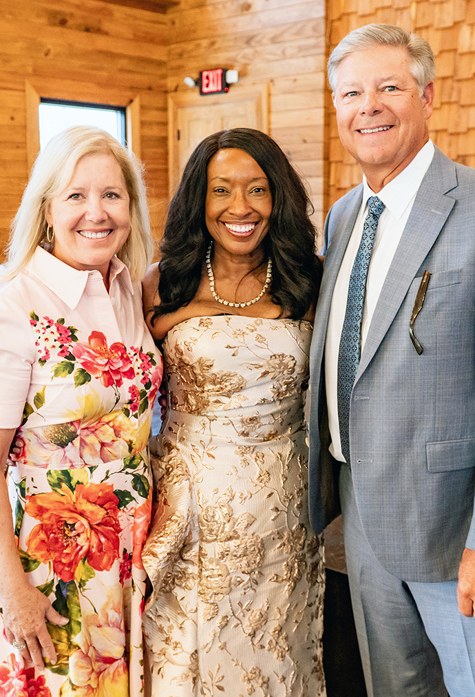 Two women and a man pose for a photo in a wood-paneled room.