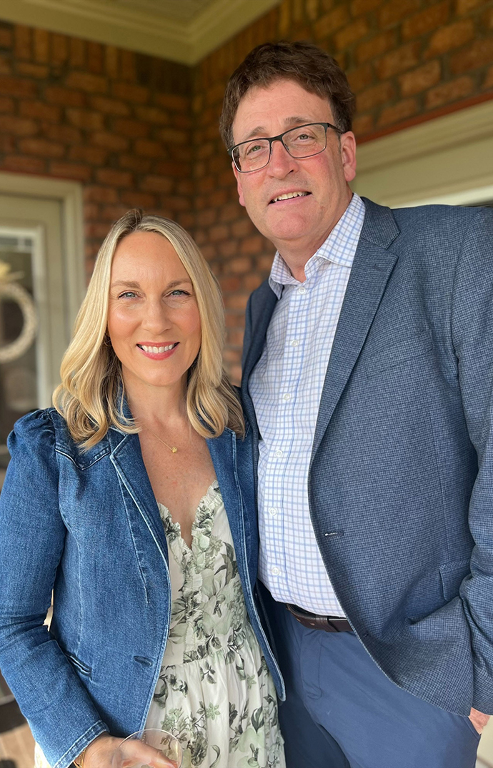 A woman and a man stand on the front porch of a house.