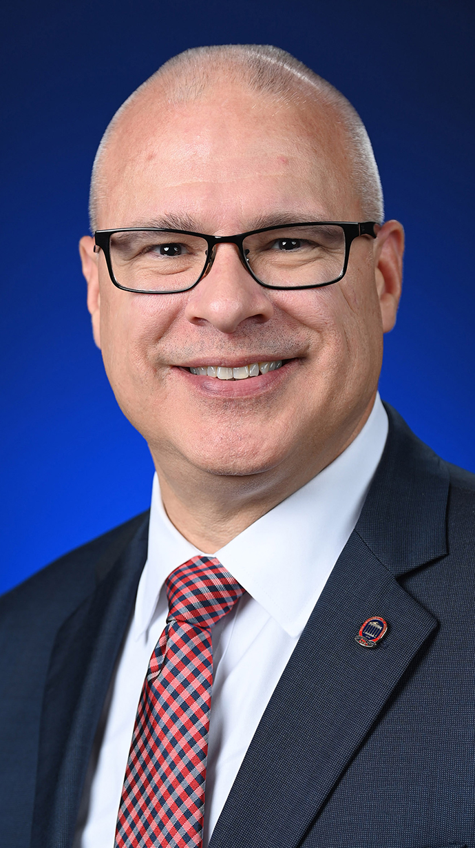 Headshot of a man wearing a dark suit nad glasses.
