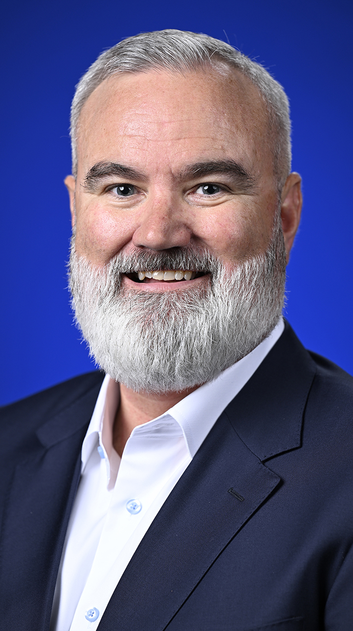 Headshot of a bearded man wearing a dark suit coat over a white dress shirt.