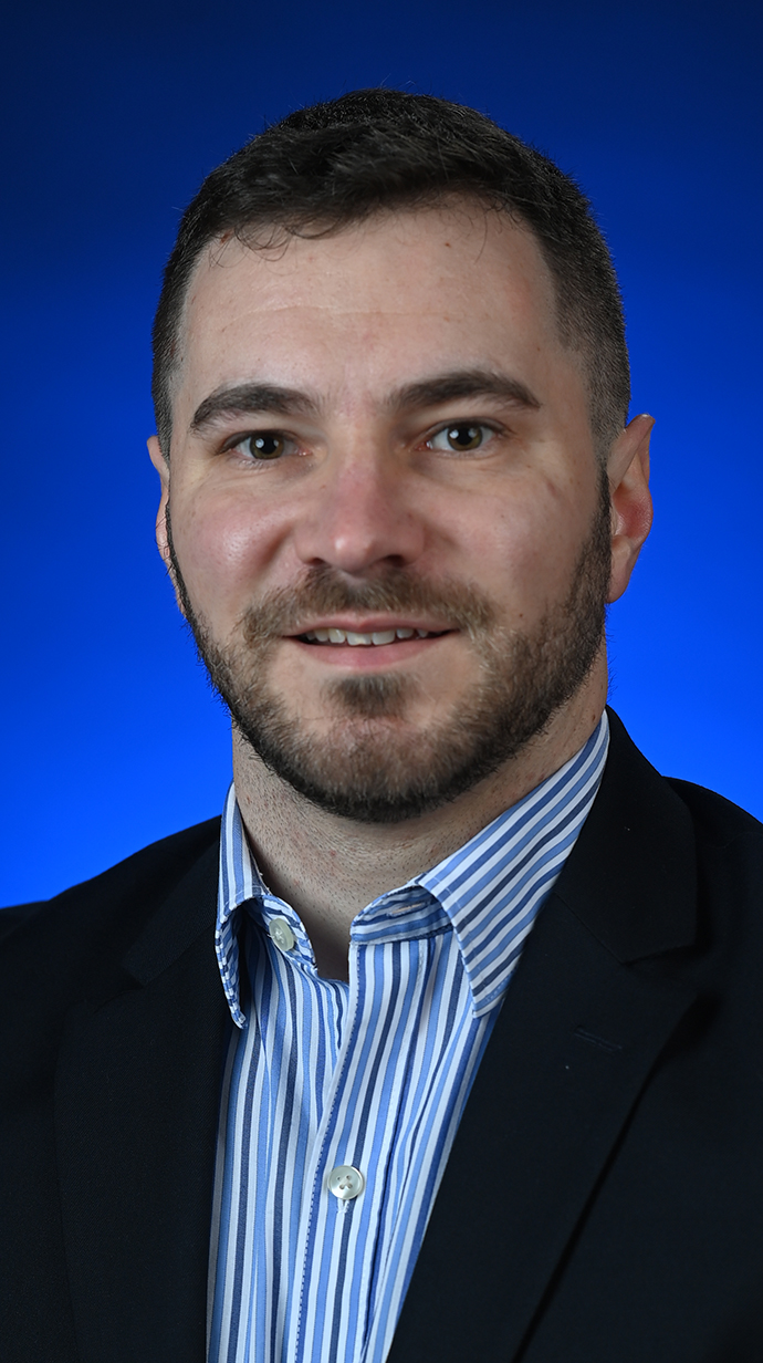 Headshot of a man wearing a dark jacket over a blue striped dress shirt.