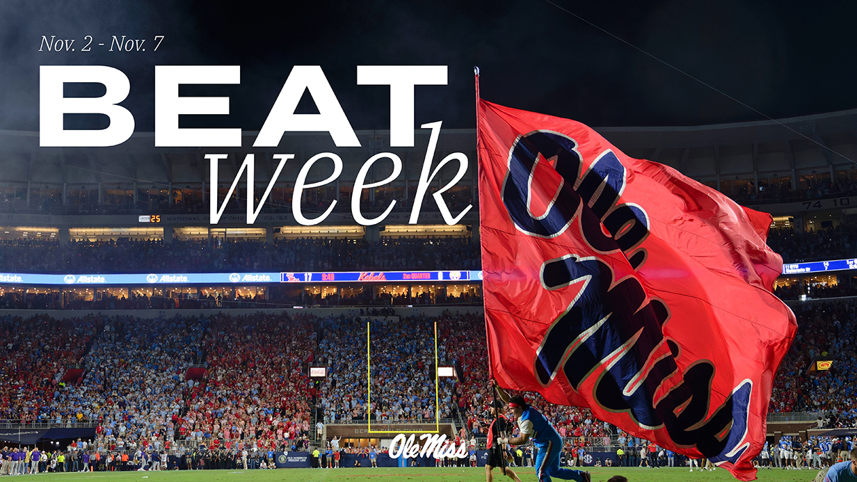 A male cheerleader carries a giant Ole Miss flag across the field in a crowded stadium with type reading 'Beat Week 2026' superimposed in front of him.