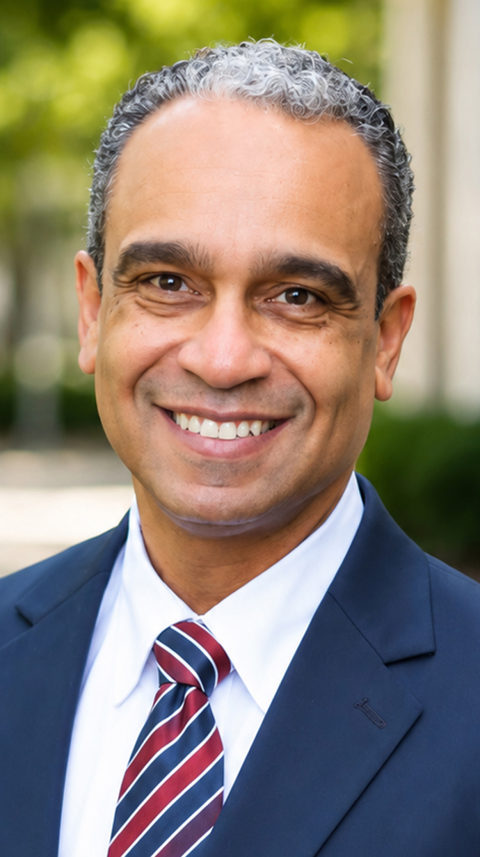 Headshot of a man wearing a dark blue suit with a red and blue tie..