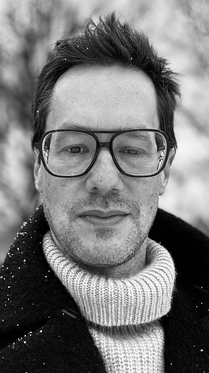 Black-and-white headshot of a man wearing a dark coat over a light-colored sweater.