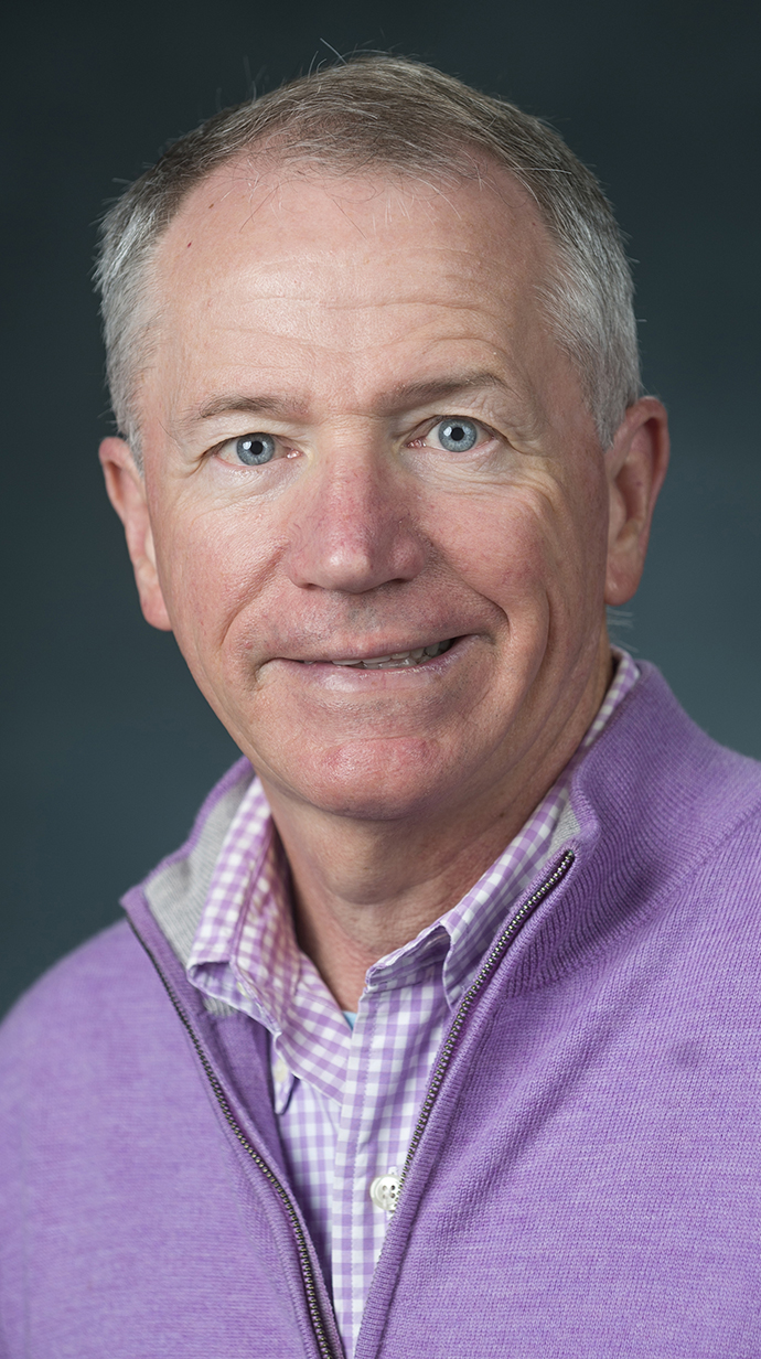 Headshot of a man wearing a lilac zippered pullover over a patterned dress shirt.