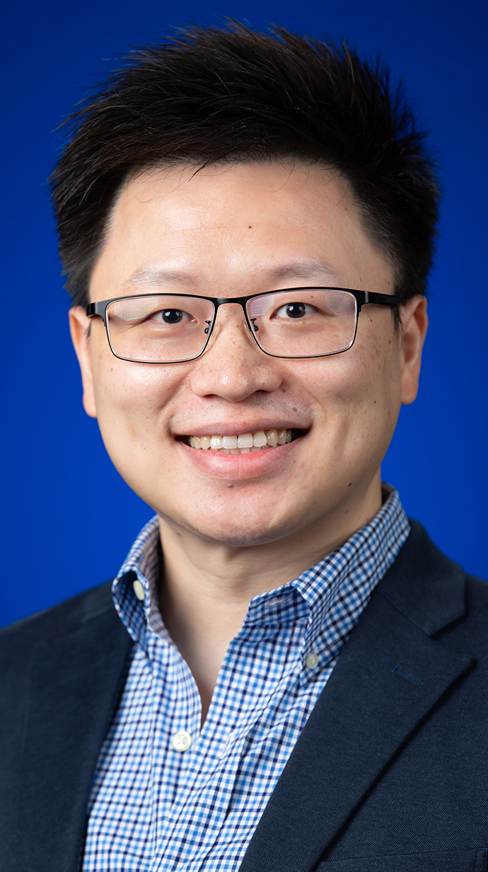 Headshot of a man wearing glasses and a dark blue jacket over a blue checked shirt.