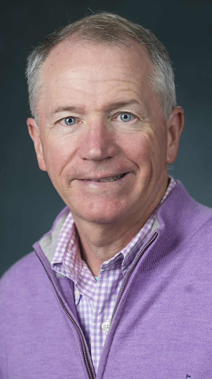 Headshot of a man wearing a lilac pullover over a light-colored dress shirt.
