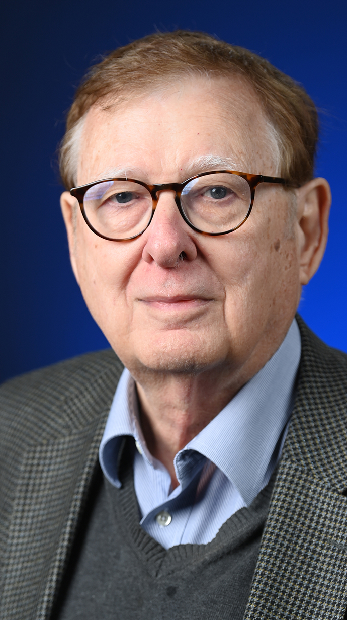 Headshot of a man wearing a tan suit with a light blue shirt.