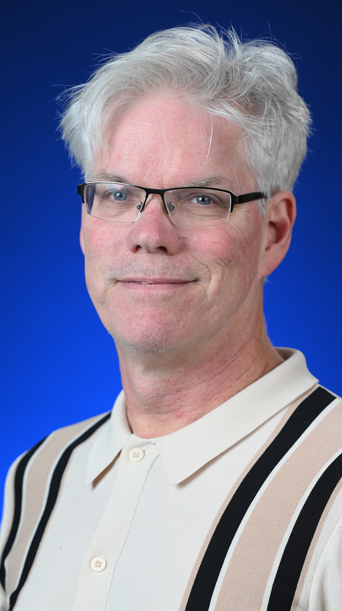 Headshot of a man wearing a casual white and tan shirt.