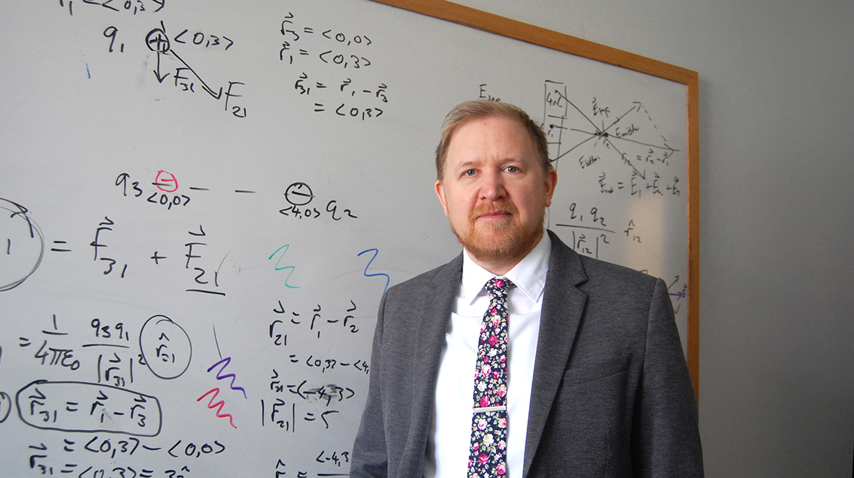 A man stands in front of a whiteboard filled with equations.