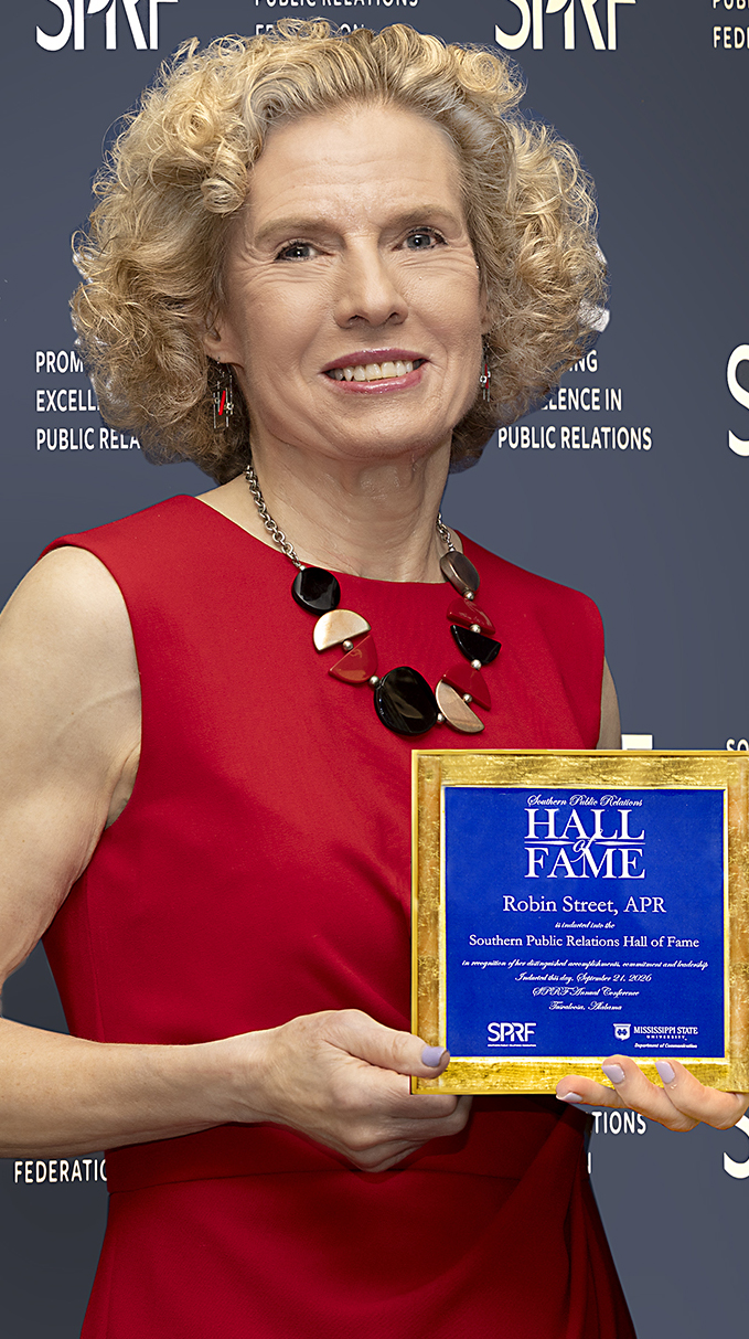 A woman wearing a red dress holds an award plaque.