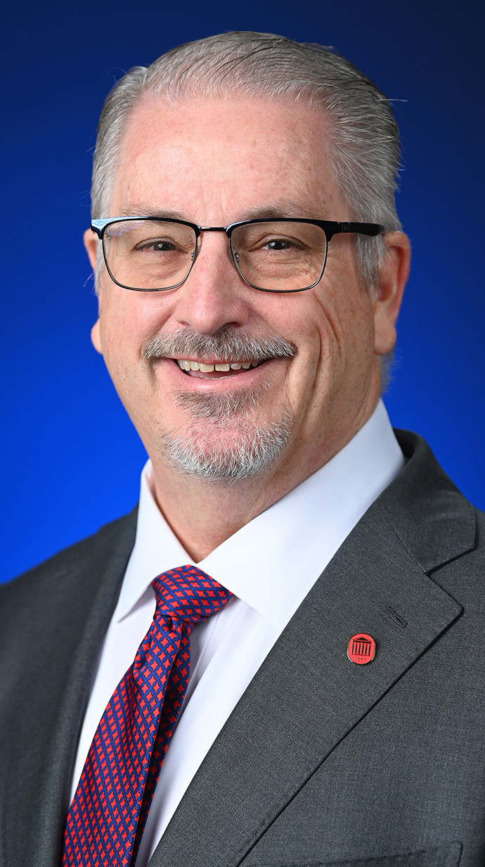 Headshot of a man wearing a gray suit with a red-and-blue tie.