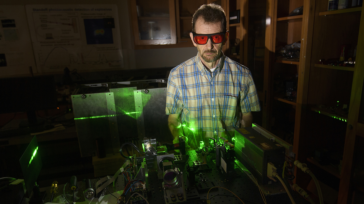 A man wearing red safety glasses works with a green laser in a darkened lab.